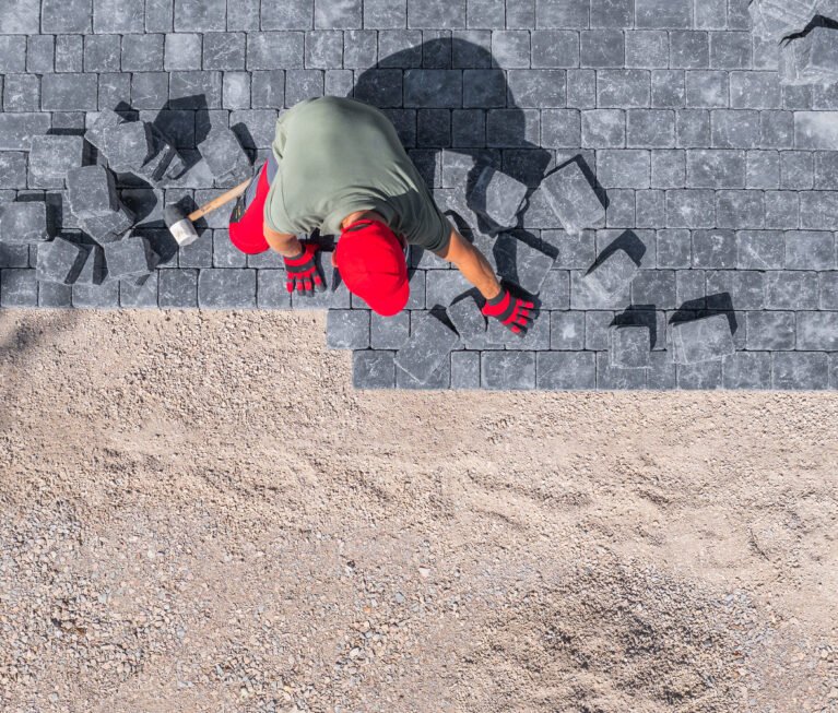 A laborer carefully positions paver stones to create a sturdy driveway in a residential setting during the day.