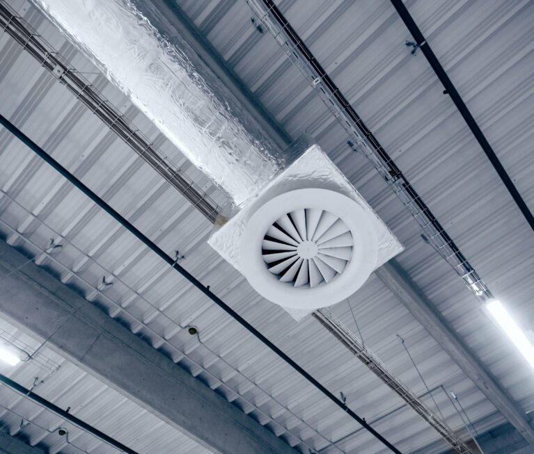 Air ventilation system on the ceiling in a large warehouse. Pipes made of silver insulating material hang from the ceiling inside the new building