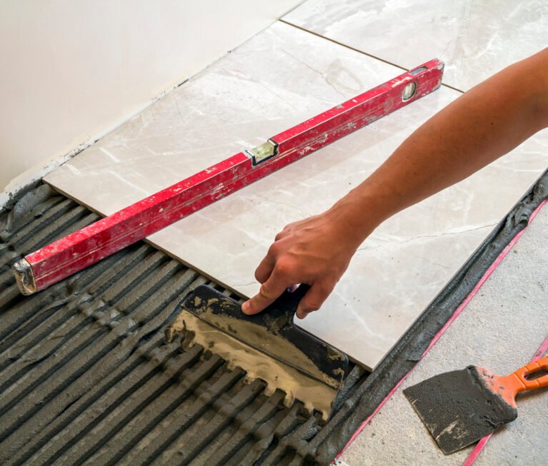 Ceramic tiles and tools for tiler. Worker hand installing floor tiles. Home improvement, renovation - ceramic tile floor adhesive, mortar, level