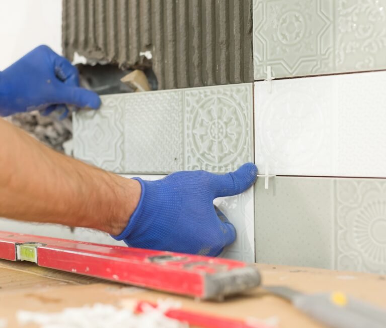 Closeup of tiler hand laying ceramic tile on wall in kitchen, renovation, repair, construction.