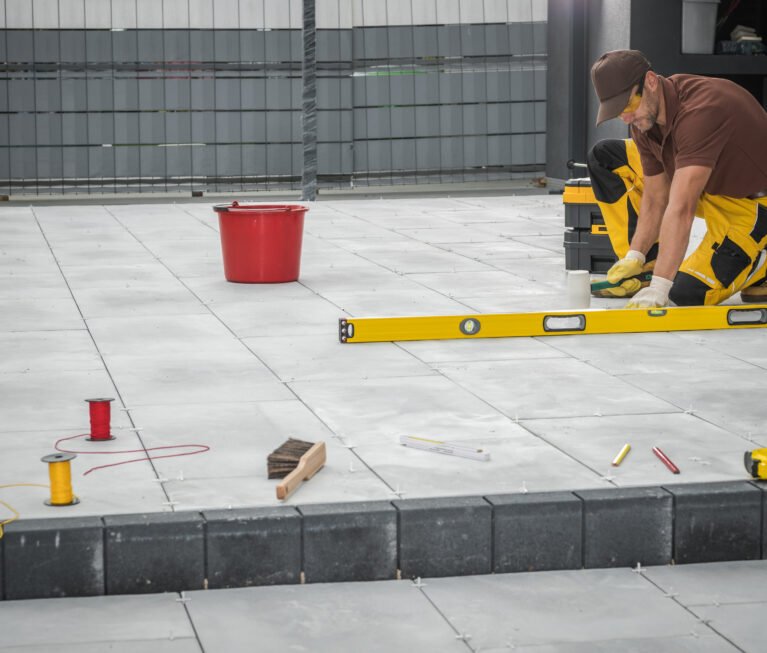Contractor Finishing Building of Concrete Porch Next to Residential House Checking the Leveling of Tiles with Large Professional Spirit Level Tool.