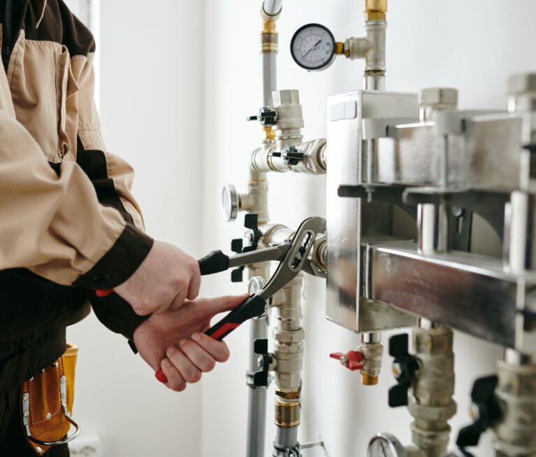 Man in plumber uniform using wrench while repairing pipe