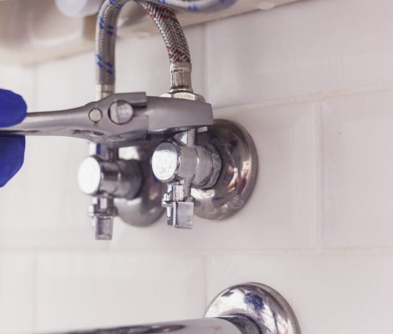 Plumber turns nut on angle valve under wash basin using spreading wrench