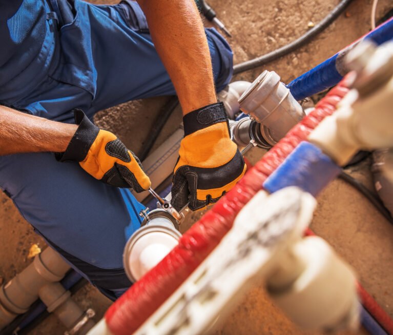 A plumber uses tools to fix piping systems in a construction setting, showcasing hands-on work and problem-solving skills in plumbing repairs.