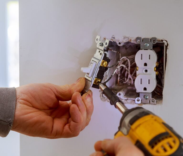 The hands of an electrician installing a power switch to the electrical junction box