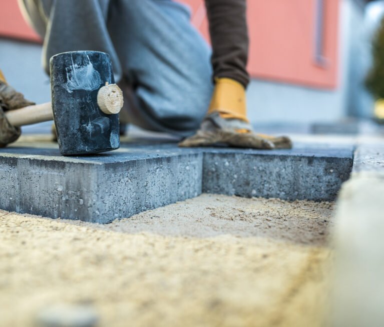 Workman tamping down a new paving brick with a mallet.